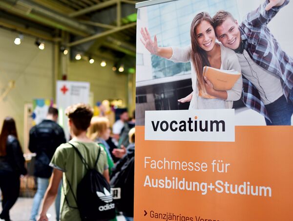 Im Vordergrund rechts im Bild ein orangefarbenes Plakat zur Vocatium Fachmesse für Ausbildung und Studium, links im Bild im Hintergrund verschwommen Menschen auf der Messe