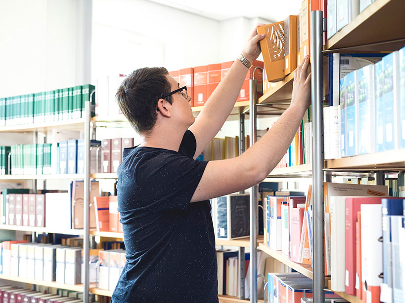 In einer Bibliothek sucht sich ein Dualer Student Fachliteratur für sein Studium heraus