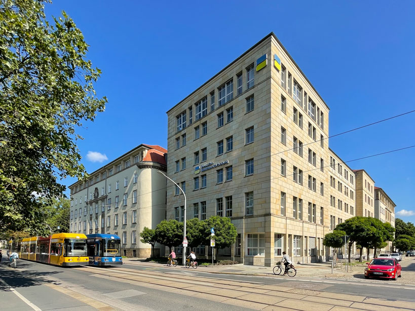 Gelbe und blaue Straßenbahn vor den beiden Gebäuden der Deutschen Rentenversicherung in Dresden