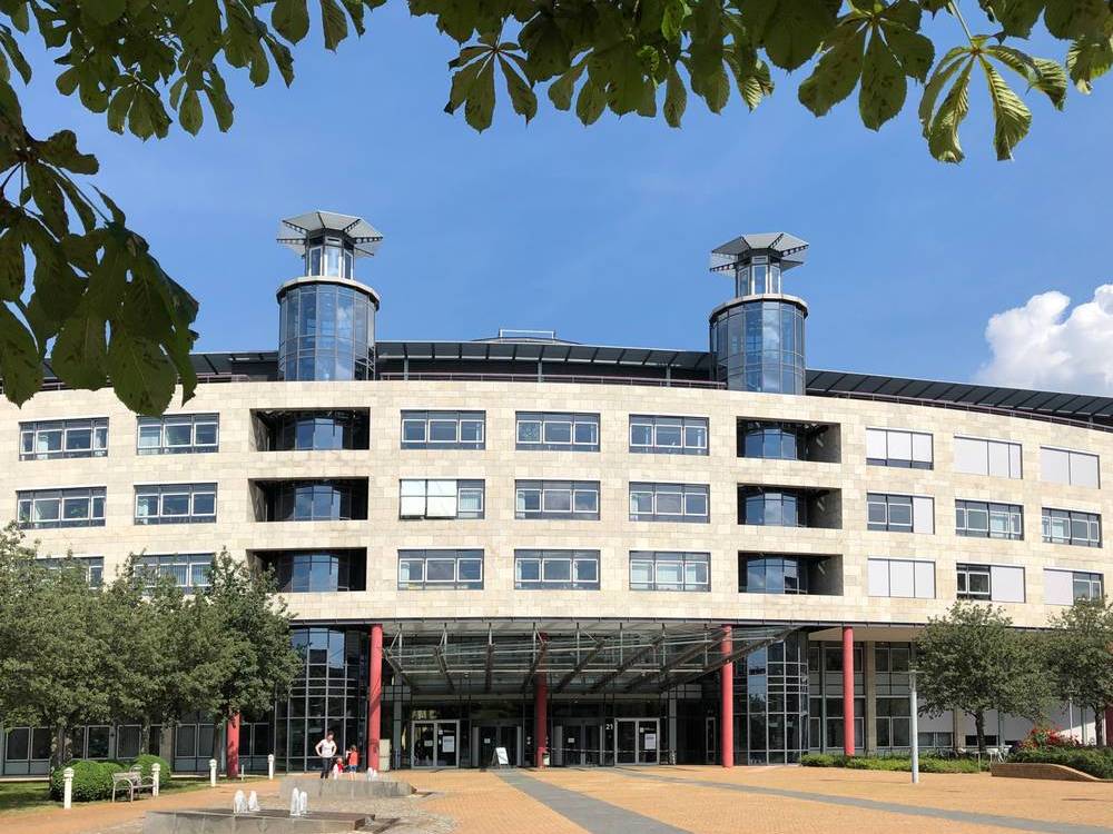 Platz vor dem Gebäude der Deutschen Rentenversicherung Mitteldeutschland in Halle (Saale) mit kleinen Springbrunnen und grünen Bäumen im Sonnenschein