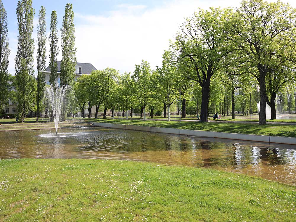 Springbrunnen, umgeben von hohen Bäumen vor dem Hauptgebäude der Deutschen Rentenversicherung in Leipzig