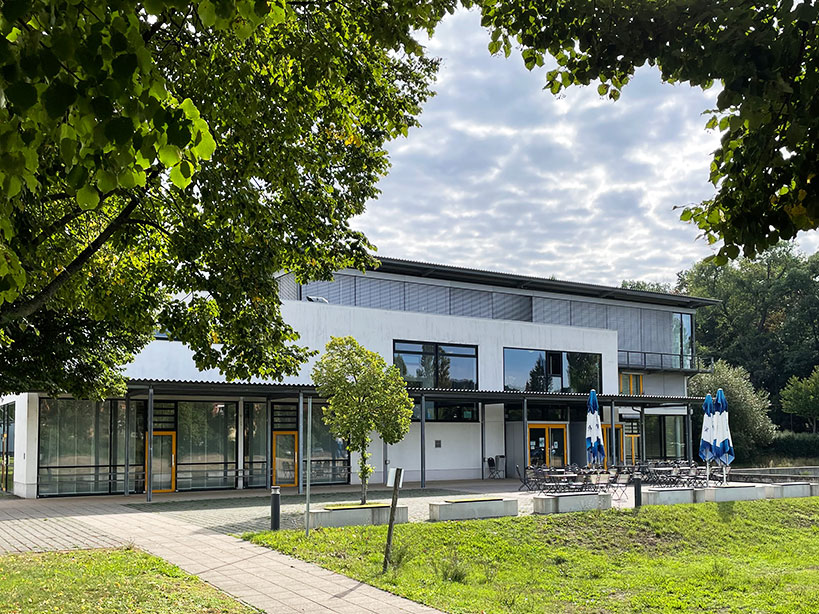 Blick durch die Bäume auf den modernen Flachbau der Mensa und Mehrzweckhalle der Hochschule Meißen