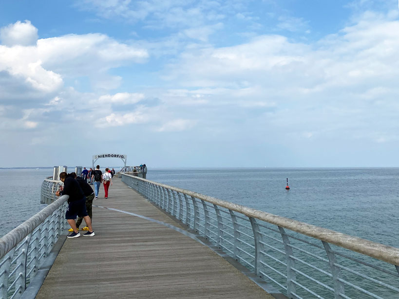 Blick vom Beginn der Seebrücke, auf der Menschen stehen und auf die Ostsee schauen